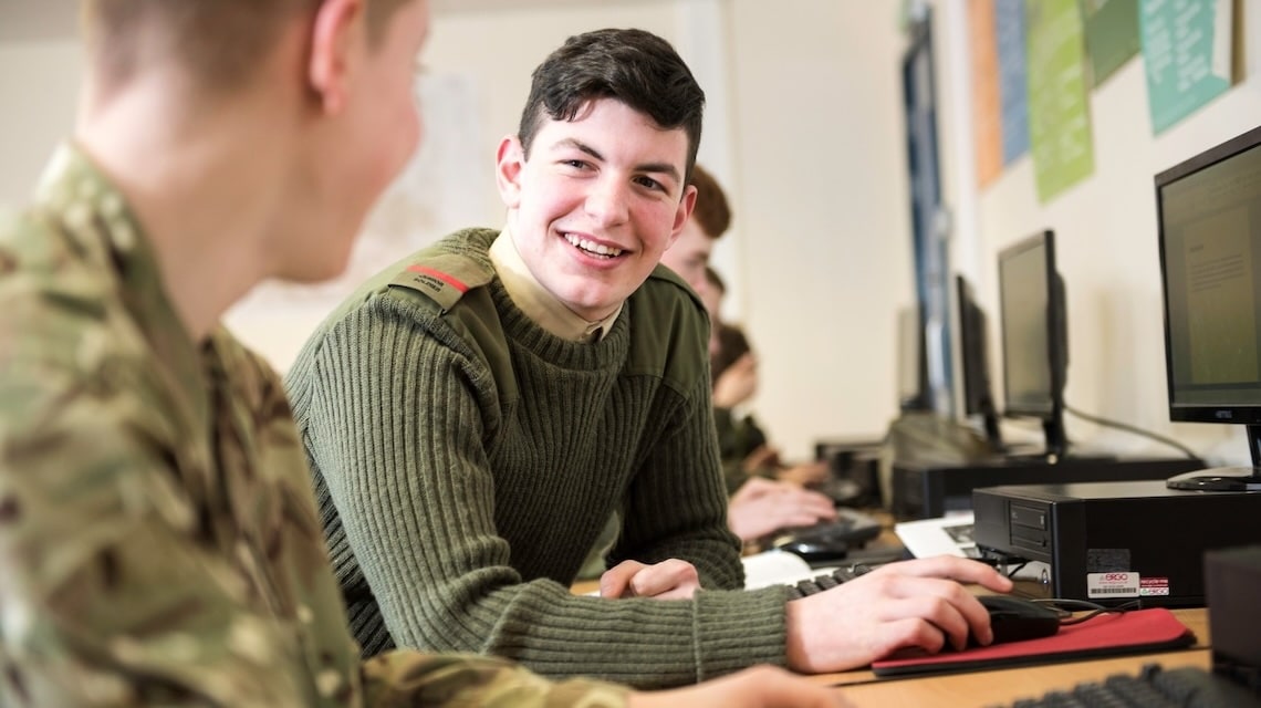 MoD learners in a computer lab working together on desktop computers, focusing on technical tasks and collaborative problem‑solving in a classroom setting.