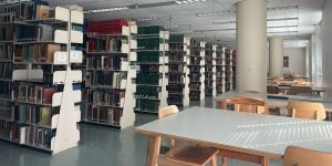 A row of tall bookcases alongside a row of study tables in a collegiate library.