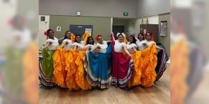 A group of college women wearing traditional Hispanic dancing costumes with white tops and colorful, ruffled skirts.