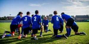 A group of college students kneeling in a huddle during a flag football game.