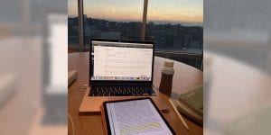 A tablet and a laptop open on a student desk with a view of campus out the window.