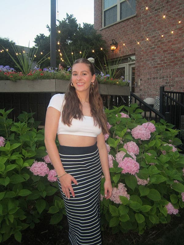 Blog author Amanda is standing outside. She has long dark hair and is wearing a long black and white striped skirt and a white crop top.