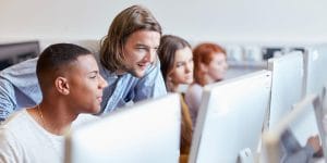 An instructor helping three college students in a computer lab.