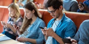 Students in a lecture hall, all looking down at their cell phone devices