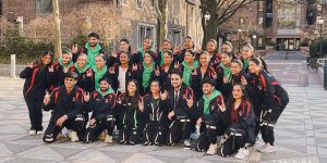 The blog author’s Bollywood dance team in a group photo. There are 27 members each wearing black track suits with red or green accents.