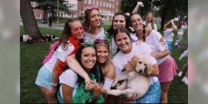 A group of sorority women are huddled together outside and smiling. One of them is holding a puppy.