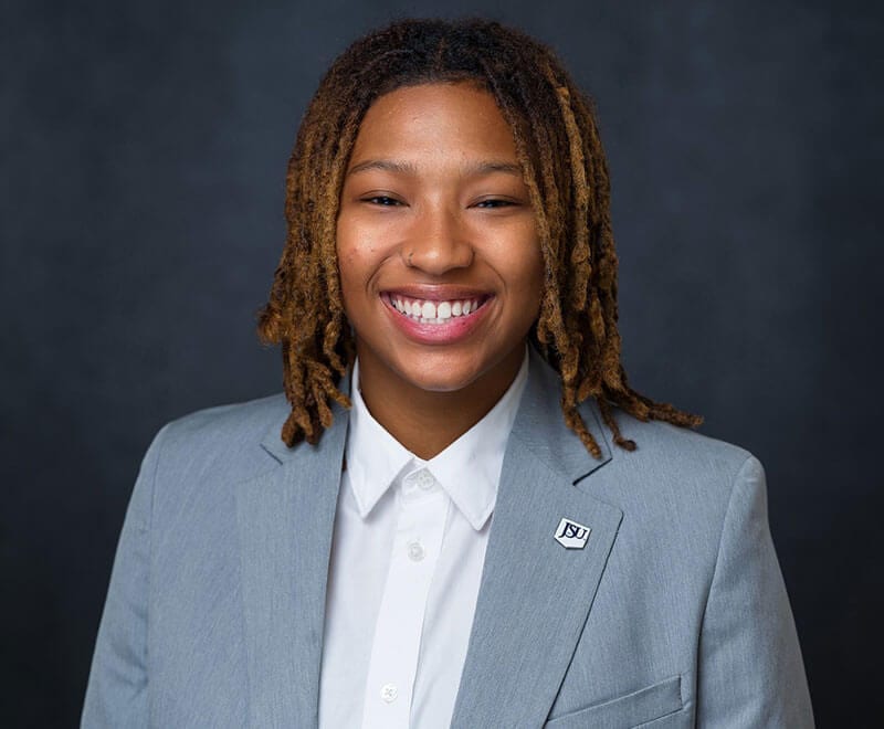 Blog author Jada has shoulder length braids and is wearing a grey blazer over a white blouse.