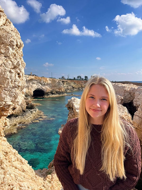 Blog author Jessica has long blonde hair and is standing outside in front of rock formations and a body of water.