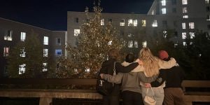 A group of four college women standing arm-in-arm looking up at a campus building at night.