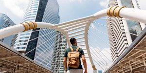 A person wearing a backpack walks through an archway between two tall buildings.