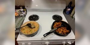 A white stove top with two pans, one with fried rice and the other with chicken cubes.