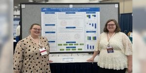 Two young college women standing on either side of a research presentation display.