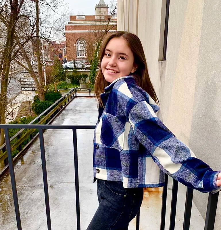 Blog author Maddy is standing outside leaning against a stair railing. She has medium length brown hair and is wearing a blue and white flannel jacket.