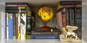 A collection of academic books on a shelf with a globe on top of the center stack of books.