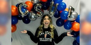 Blog author Mia is wearing a Cal State Fullerton sweatshirt and standing under a balloon arch with orange and blue balloons.