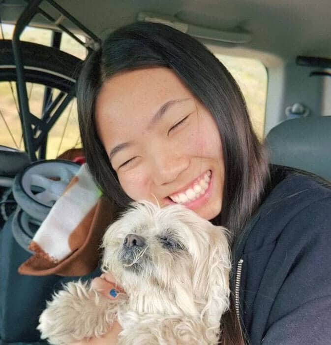 Blog author Megan is smiling and sitting in a vehicle hugging a small dog.