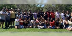 A large group of college students gathered in an outdoor space. Several are hold up hand signs representing their Greek organization.