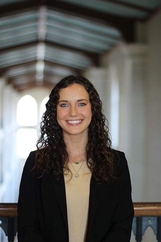 Blog author Maeve has dark curly hair and is wearing a dark blazer over a tan shirt.