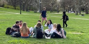 A group of students sitting in a circle and talking outside on a college quad.