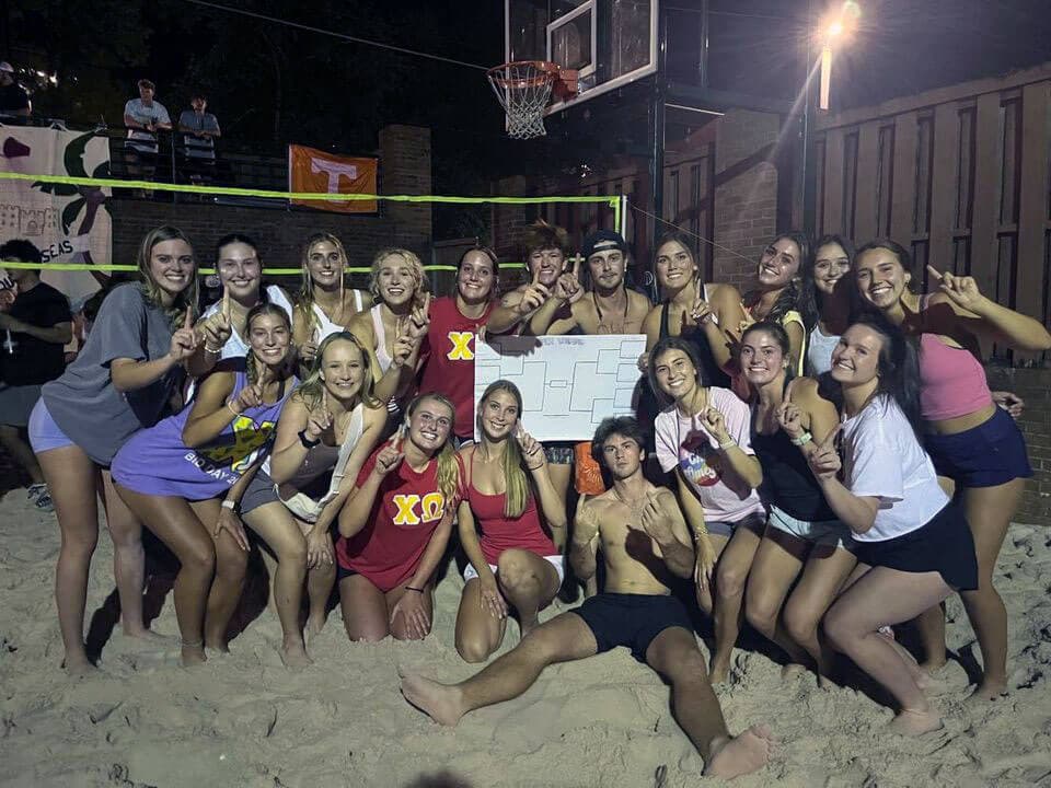 A co-ed group of college students on a sand volleyball court.