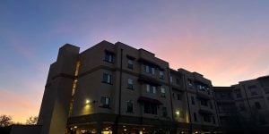 A 3-story off-campus apartment building with a blue sky and sunset behind.