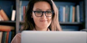 Young woman with glasses looking at laptop screen. 