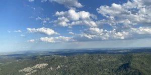 A vista of forested hills and blue sky with white puffy clouds.