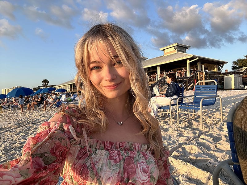 Blog author Taylor is outside on the beach. She has long wavy blond hair and is wearing a floral top.