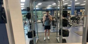 A male college student standing behind a weight set in the gym.