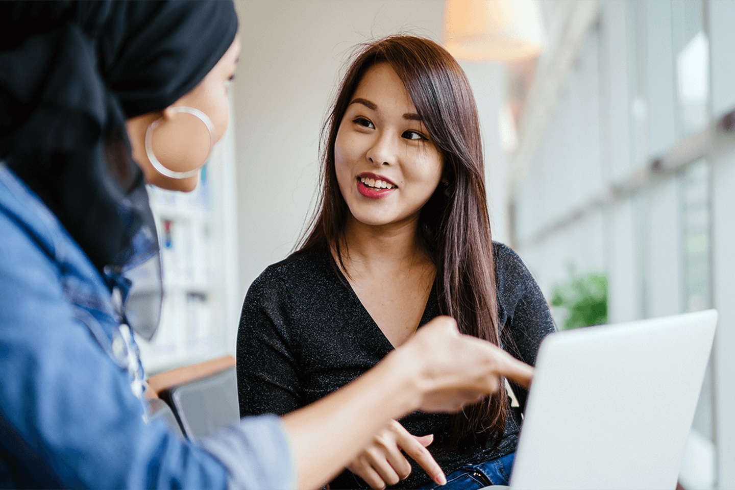 Woman pointing to laptop, teaching another woman.