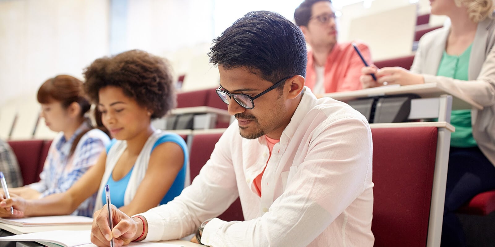 A group of higher education students sitting at desks and writing on papers
