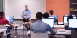 Instructor sitting at the head of a class of adult students on computers