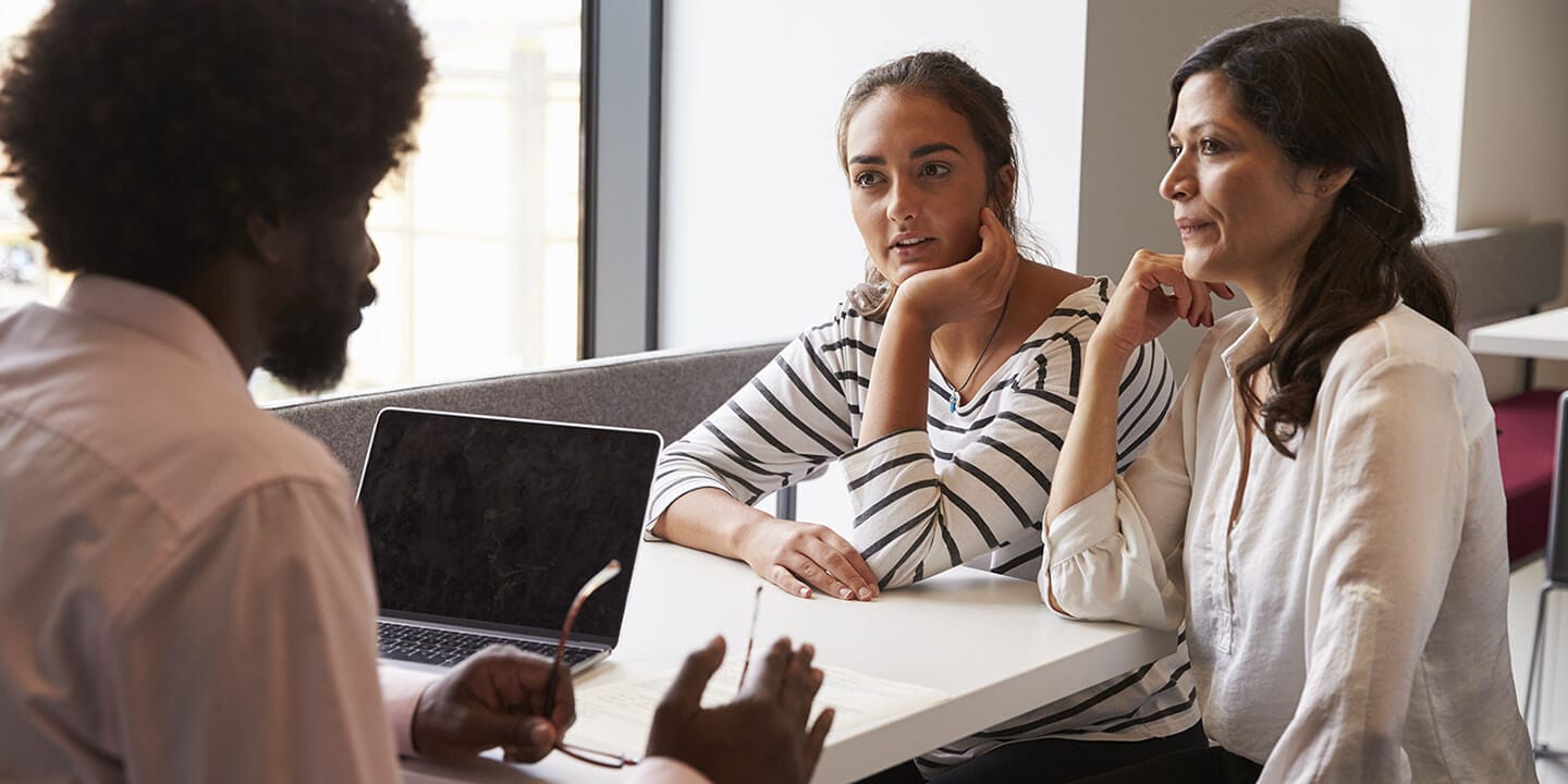 Three people sitting at a desk, having a conversation.