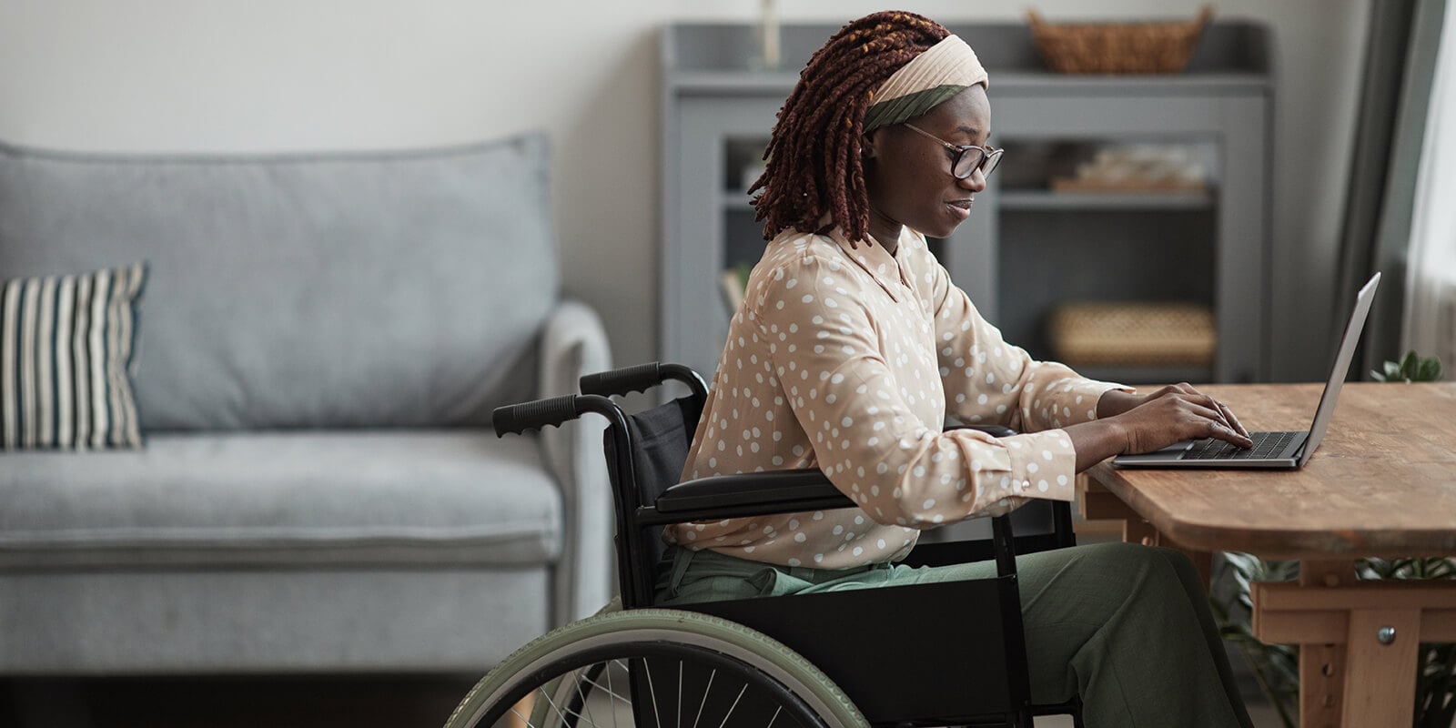 A woman sitting at the table in a wheel chair and working on laptop.