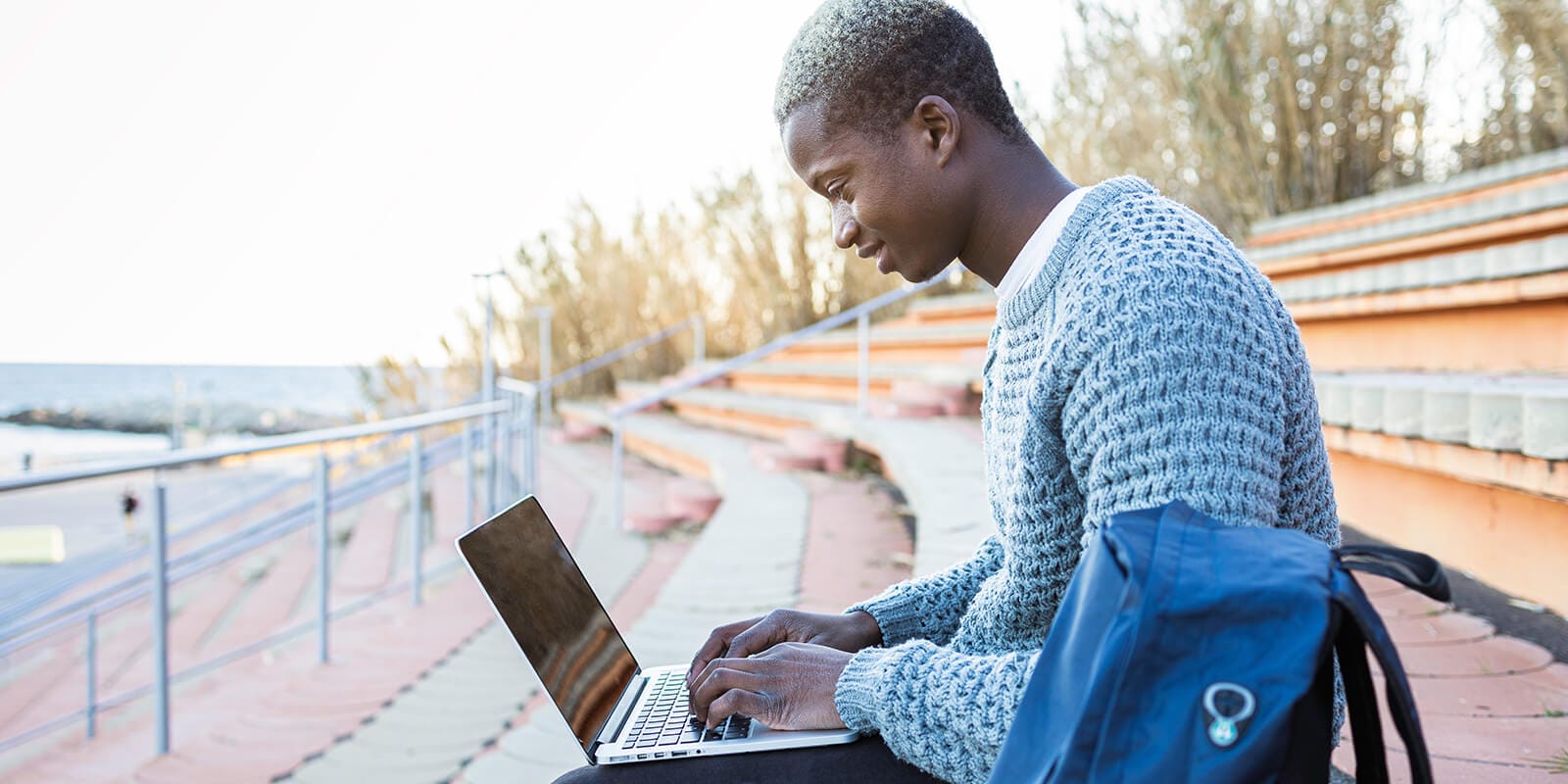 A man is sitting on a bench and working on a laptop.