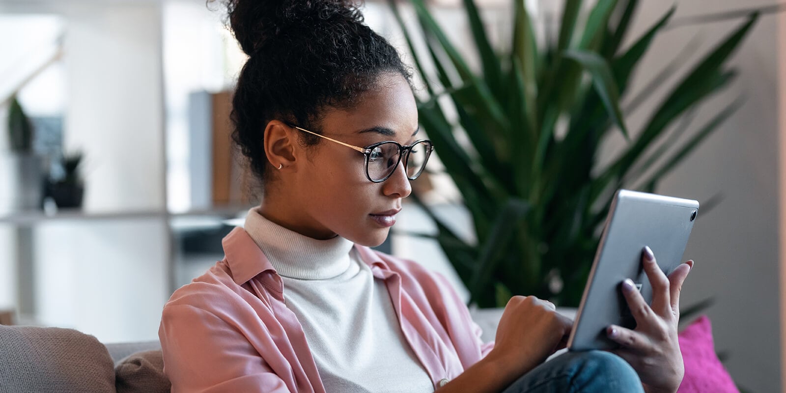 A woman looking sitting on a couch and looing at a device screen