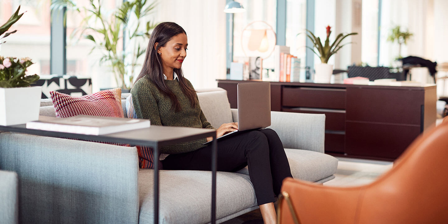 A woman sits on a sofa, working on a laptop computer.