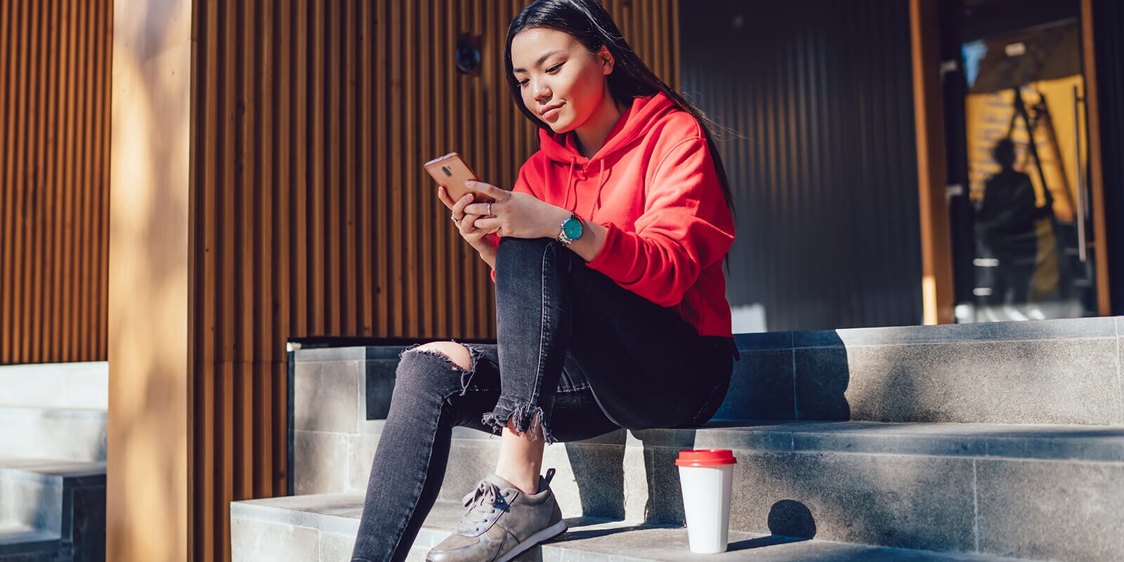 Young woman outside on the steps looking at her smartphone