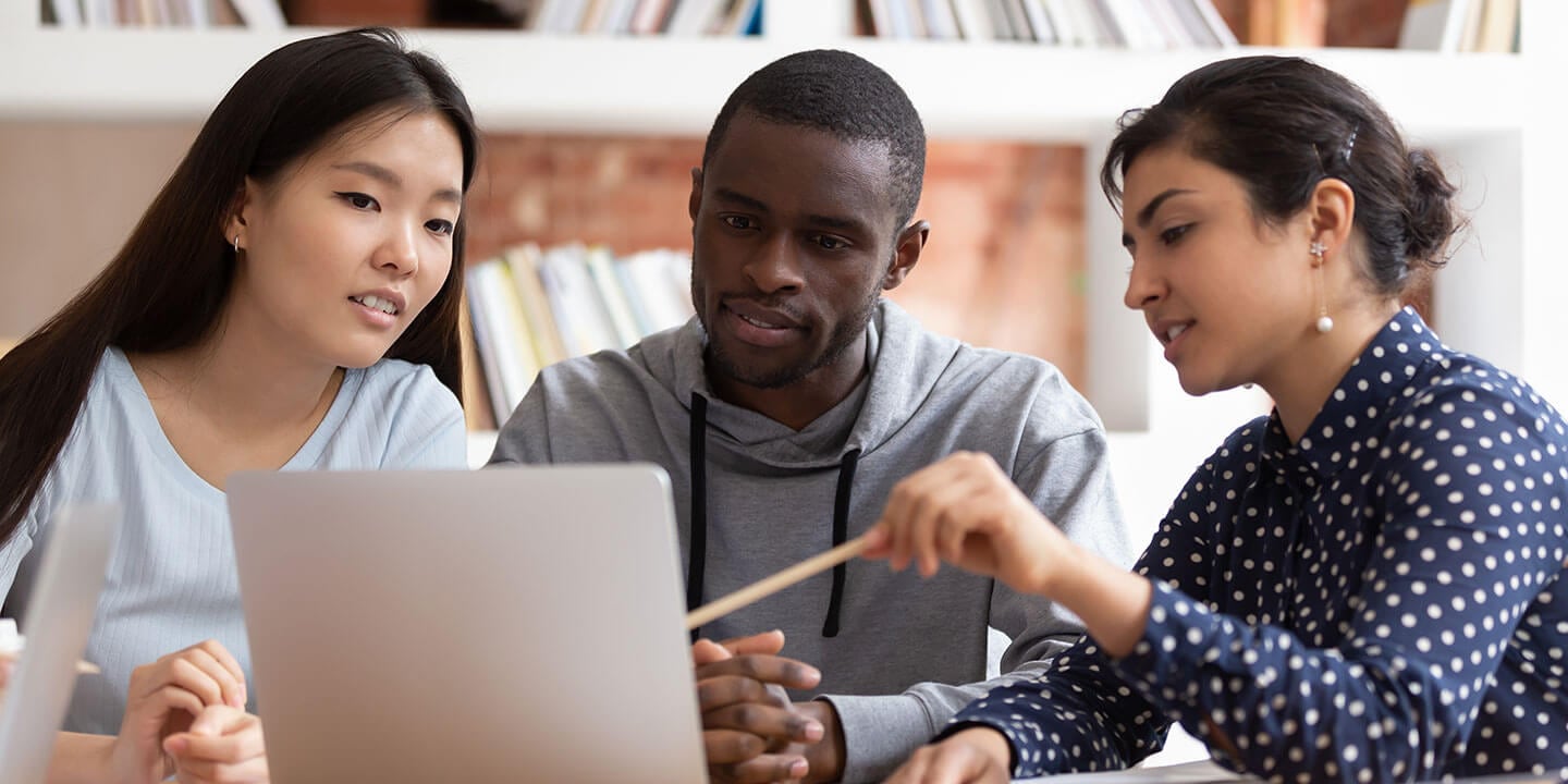 Three students are looking at a laptop screen and discussing the contents.