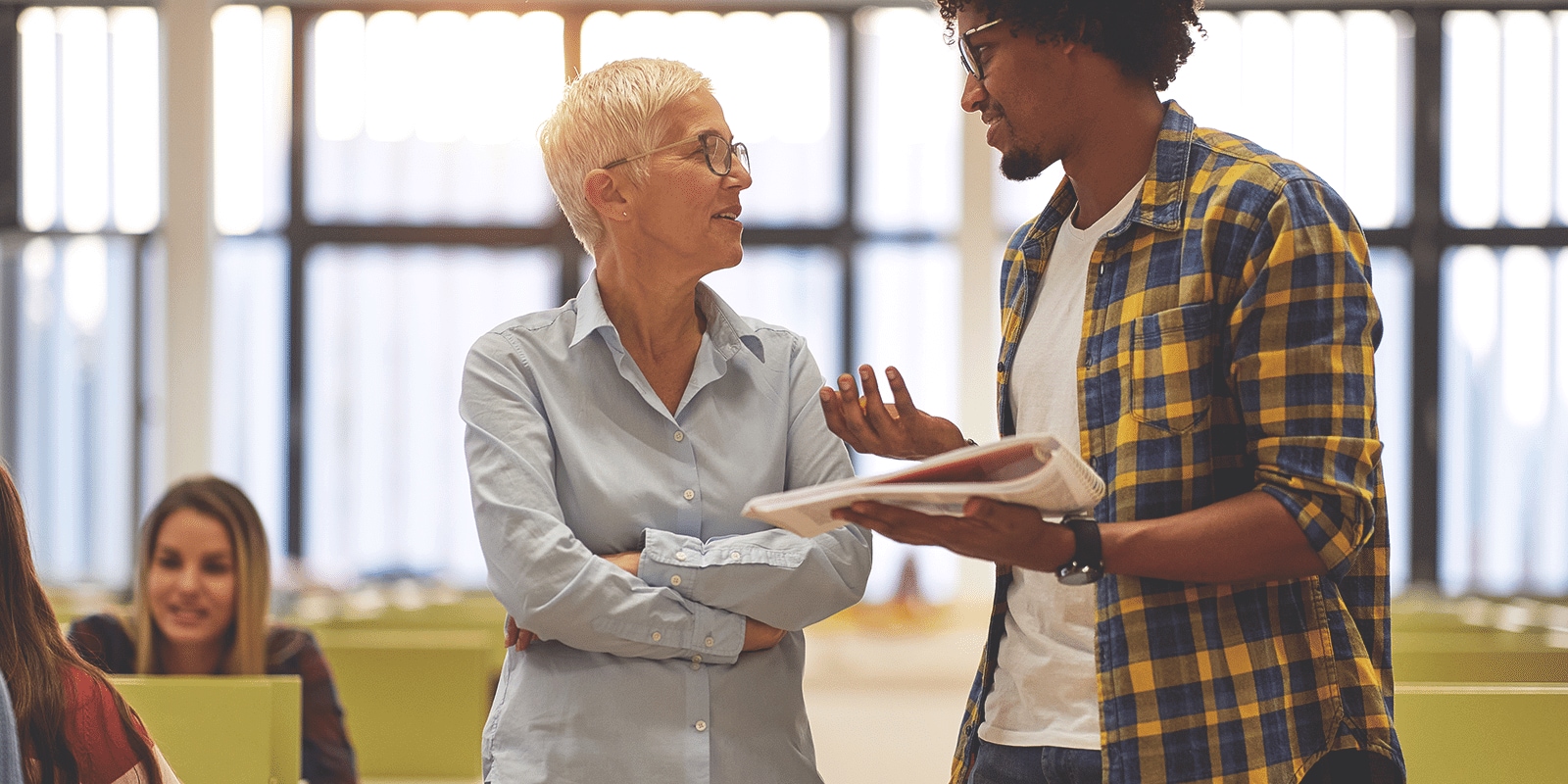 A student talking to instructor holding a book in his hands.