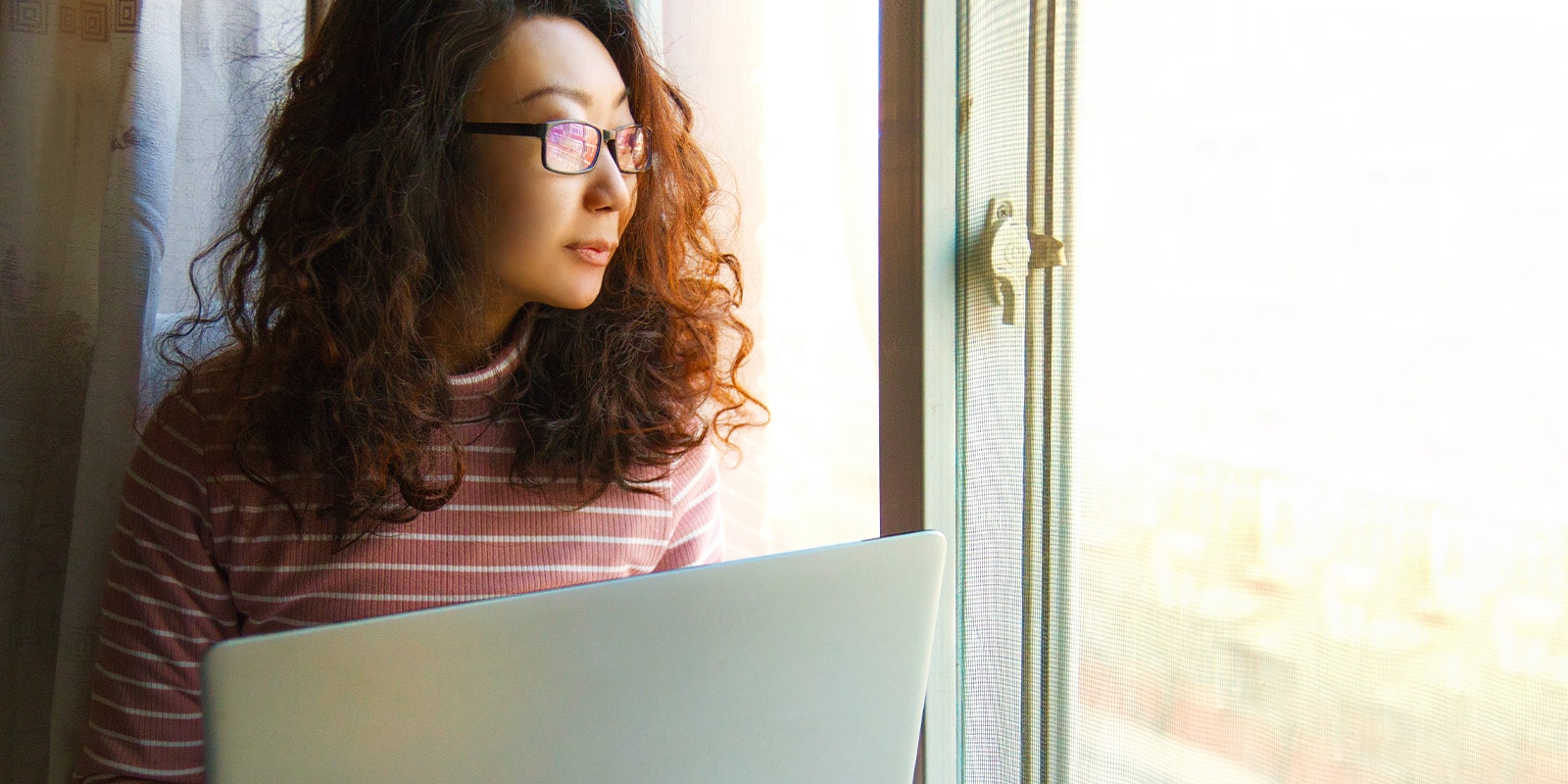 You woman holding laptop looking out her window