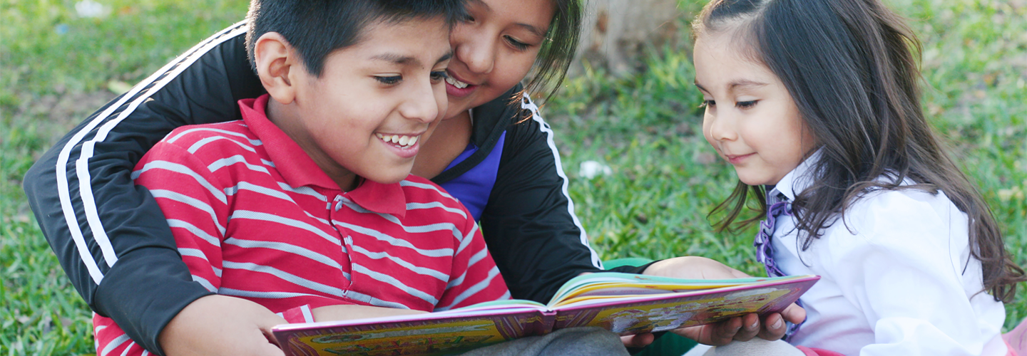 Children sat outdoors reading a book together