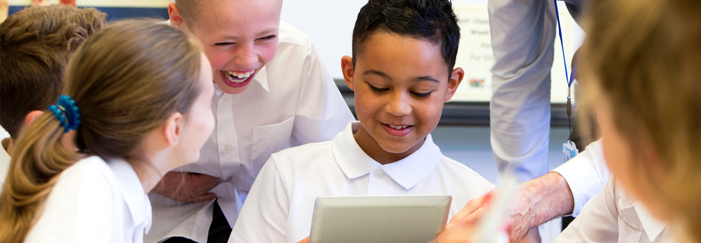 Children and teacher looking at a tablet smiling and laughing in the classroom