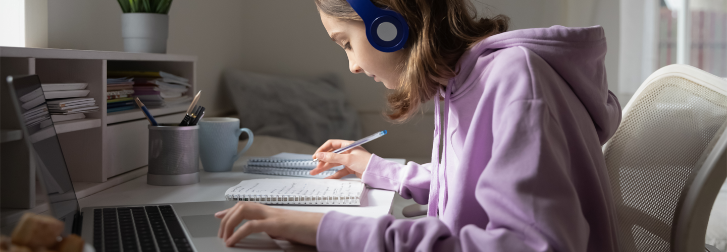 A girl sat at a desk with a laptop and notepad studying and taking notes