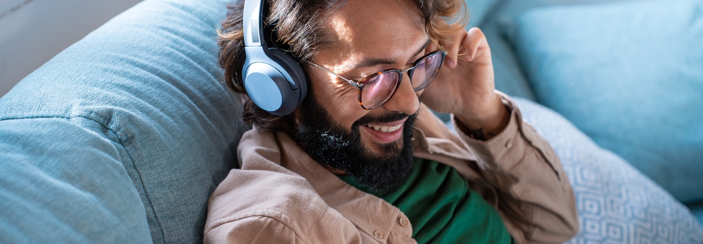 A man with headphones on listening and smiling while he sits on a sofa