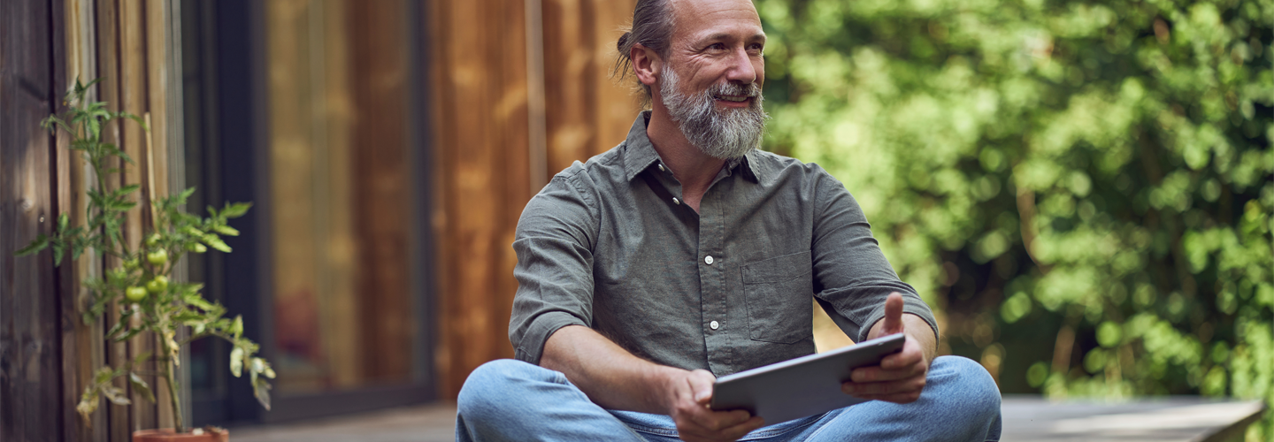 Man sat outdoors holding a tablet smiling