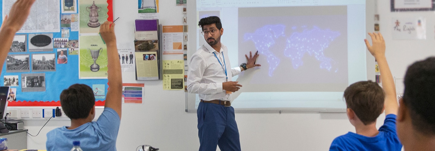 A teacher working on a interactive whiteboard and students raising their hands