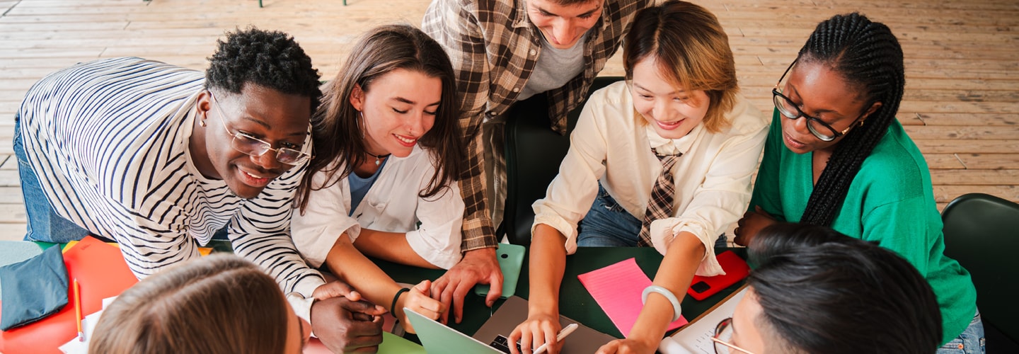 A group of teenagers working on a activity gathered around a table smiling