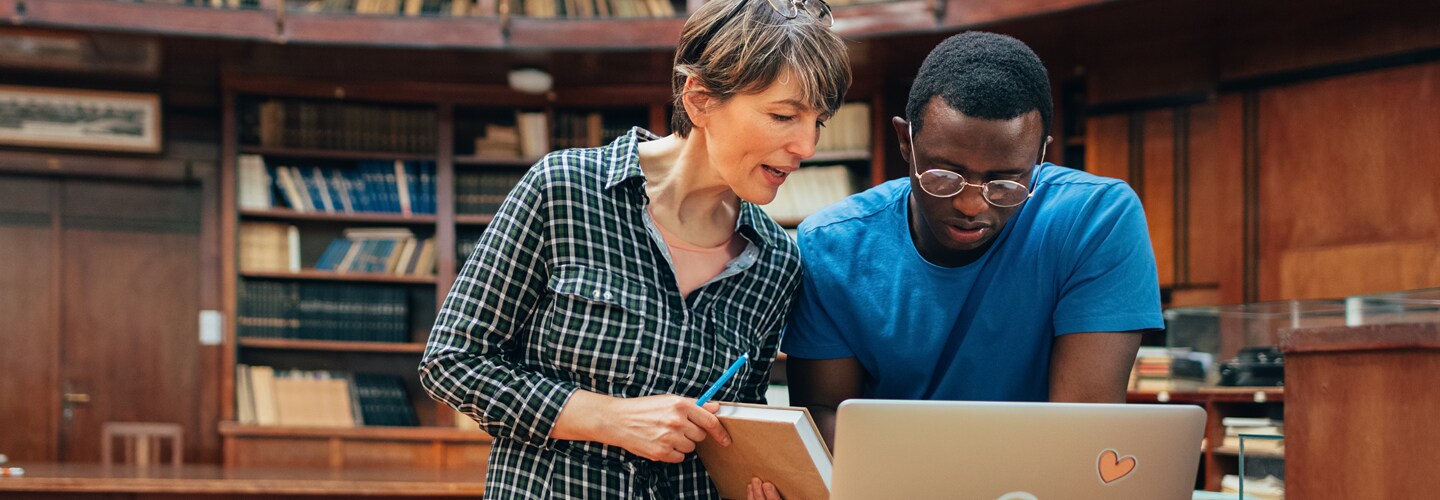 A woman and man working together on laptop in library