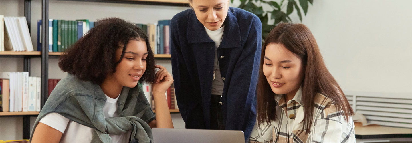 A teacher looking at a laptop with two female students